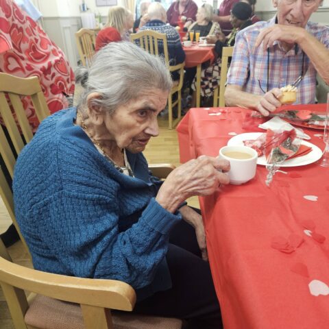 Resident in a blue cardigan drinking tea at a red table decorated with hearts