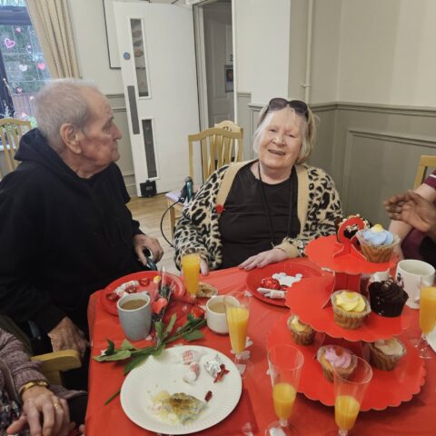 Residents chatting around a red table with cupcakes tea and heart decorations