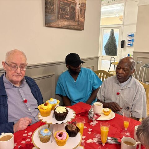 Three residents seated at a red decorated table with cupcakes tea and orange juice