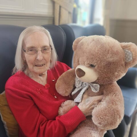 Smiling resident in a red top holding a large brown teddy bear
