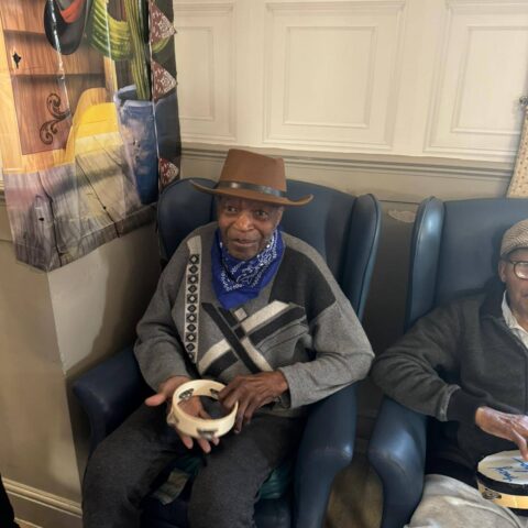 Resident seated in the lounge wearing a brown cowboy hat during a themed event