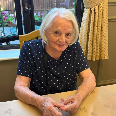 Resident smiling while seated at a table beside the garden windows