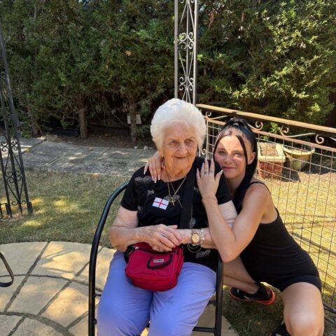 A resident sitting outdoors with a family member kneeling beside them, sharing a friendly hug in the garden.