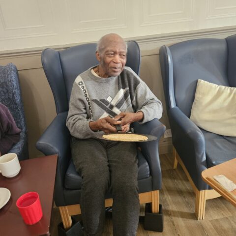 Resident seated in a lounge chair holding and playing a small string instrument