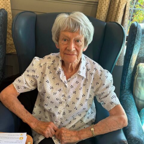 Resident sitting comfortably in a blue armchair in the care home lounge