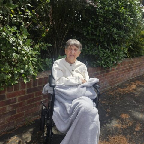 Resident smiling in a wheelchair beside garden greenery at Nightingale Care Home