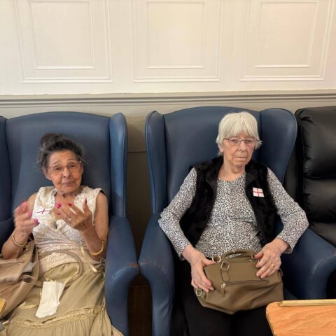 Two residents seated indoors wearing England flag badges during the World Cup celebration.