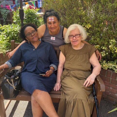 Residents and staff sitting together on a garden bench during the summer party, surrounded by flowers and decorations.