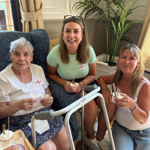 Residents enjoying small cups of ice cream indoors, wearing England flag badges during the World Cup celebration.