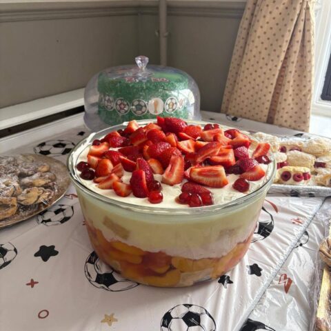 Large trifle bowl and assorted desserts displayed on a football-themed tablecloth at the summer party.